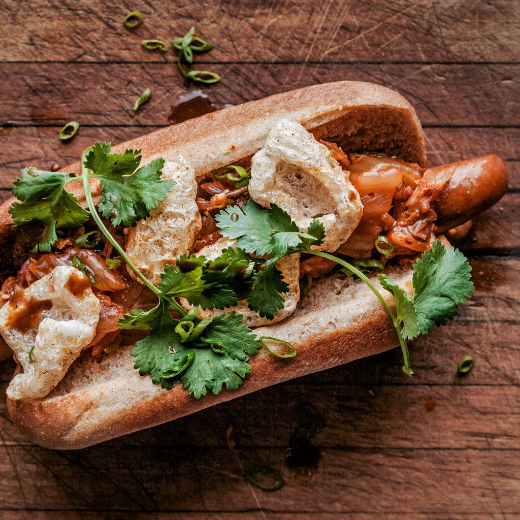 Hot dog topped with kimchi, chicharrones and cilantro 
