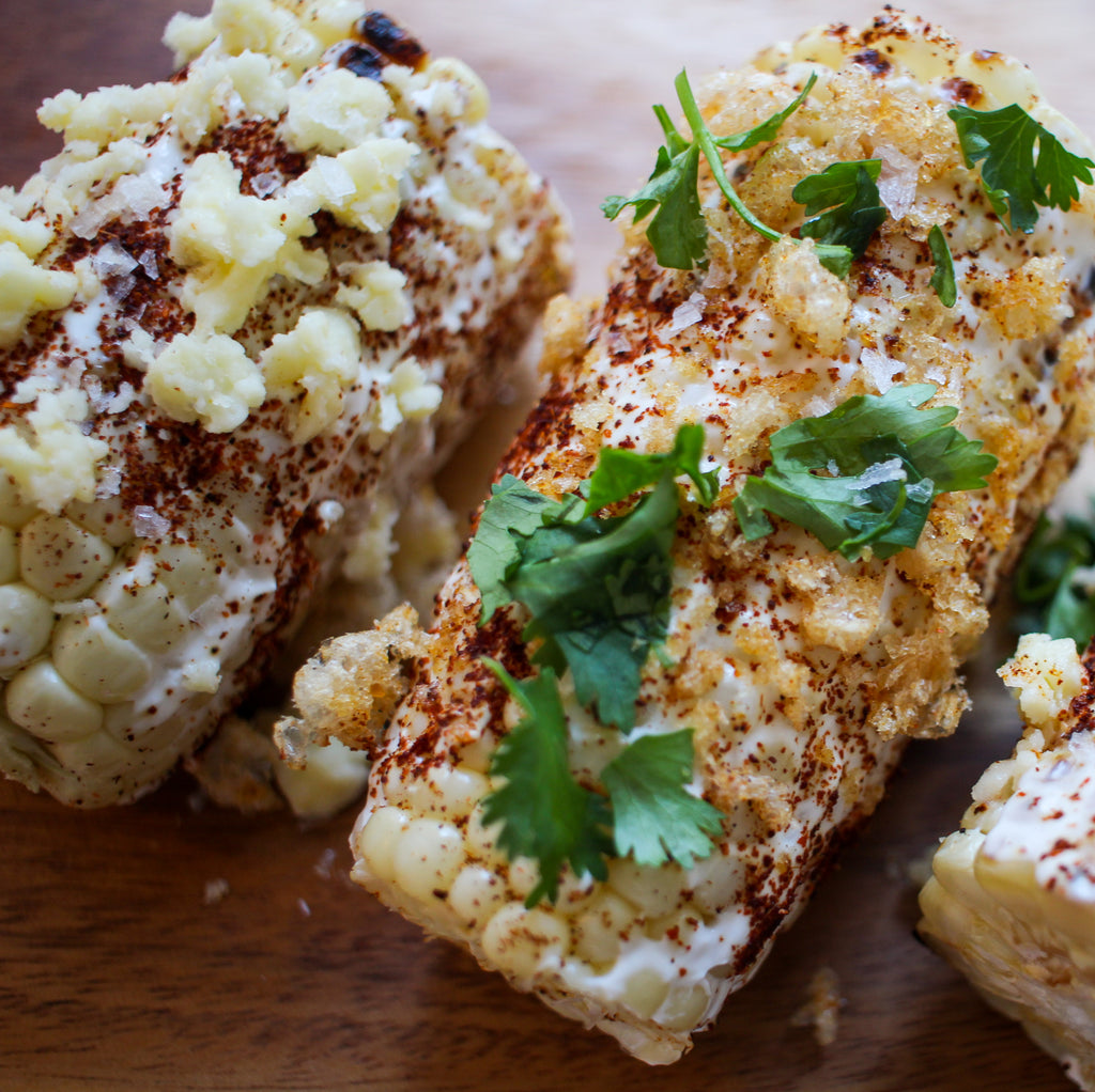 Corn on the cob topped with crumbled cheese and chicharrones and a sprinkle of chili powder
